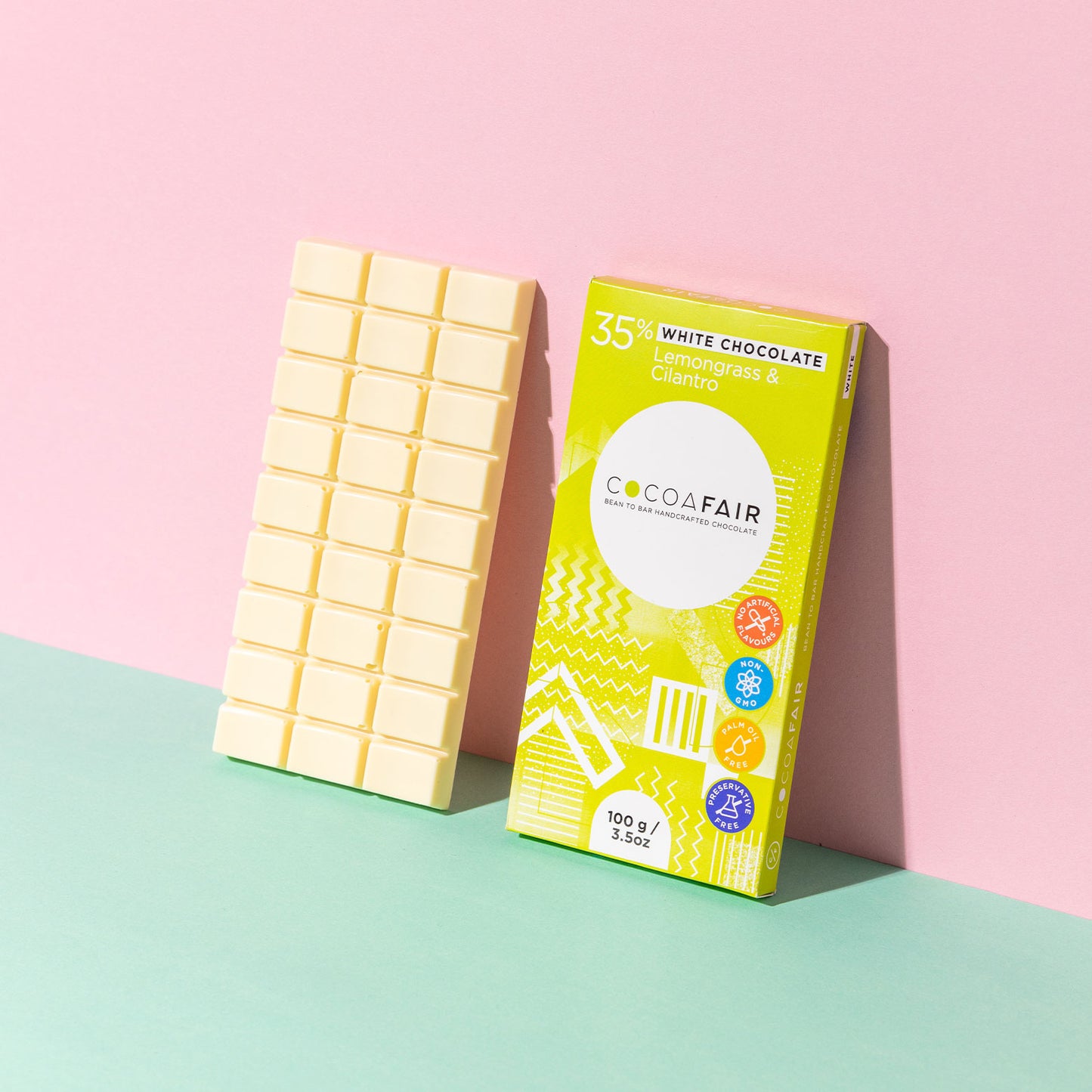 COCOAFAIR 100g 35% White Chocolate Lifestyle shot - Lime packaging on pink and green background with a slab of white chocolate. Lemongrass & Cilantro flavoured chocolate